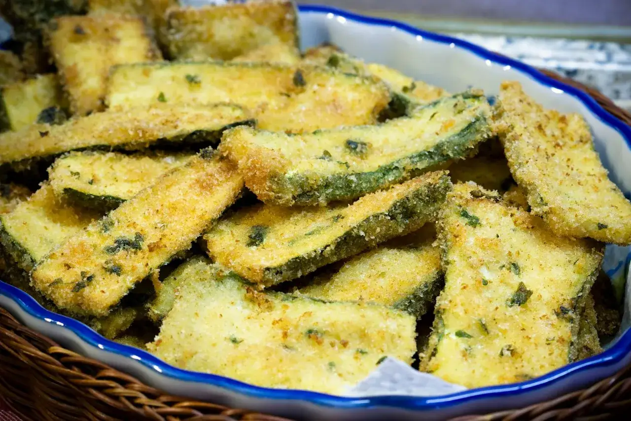 Zucchine gratinate in padella, dorate e croccanti, servite in una ciotola blu.