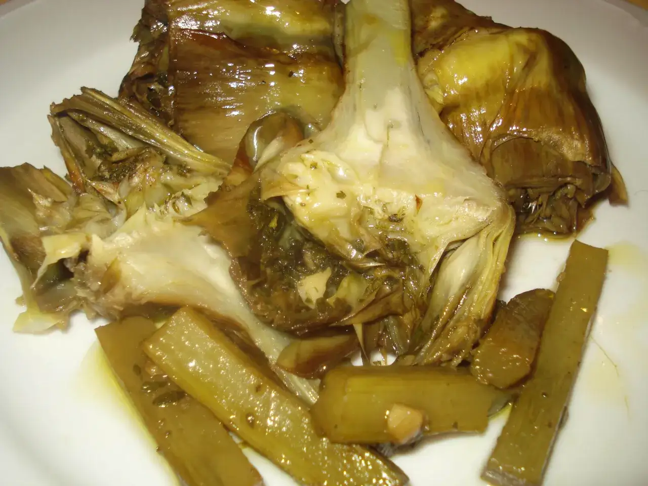 Carciofi alla romana teneri e succulenti, conditi con erbe aromatiche e olio, serviti su un piatto bianco.