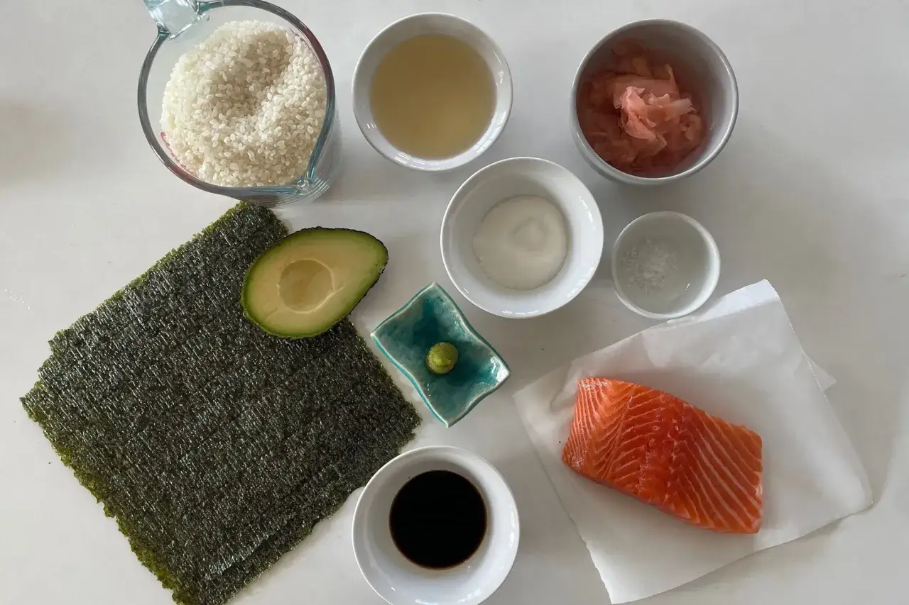 Ingredienti per sushi fatto in casa: riso, salmone, avocado, alga nori, salsa di soia, wasabi, zenzero marinato, aceto di riso e sale.
