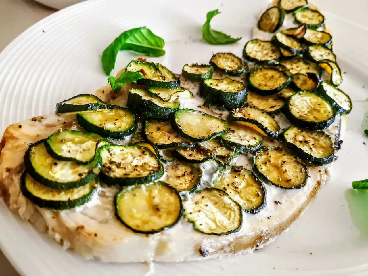 Delizioso pesce spada al forno con zucchine grigliate e una crema leggera, guarnito con foglie di basilico fresco.