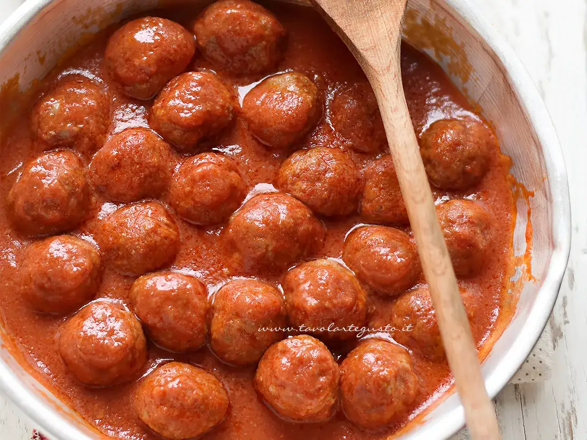 Polpette al sugo in una ciotola bianca, con un cucchiaio di legno. Un piatto invitante e saporito.