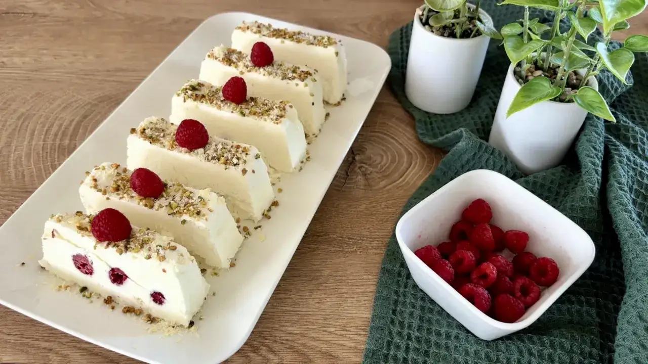 Fette di semifreddo al cioccolato con lamponi e granella di pistacchi su piatto bianco.
