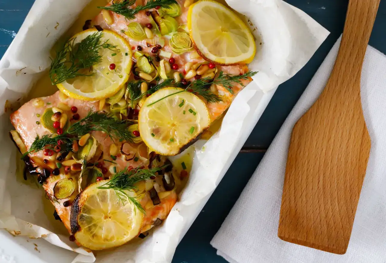 Salmone al forno succulento con limone, erbe aromatiche, pinoli e pepe rosa. Un piatto invitante pronto per essere gustato.