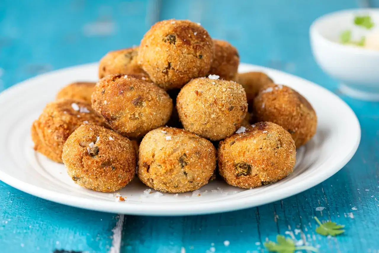 Polpette tonno e ricotta dorate e croccanti, impilate su un piatto bianco, pronte per essere gustate.