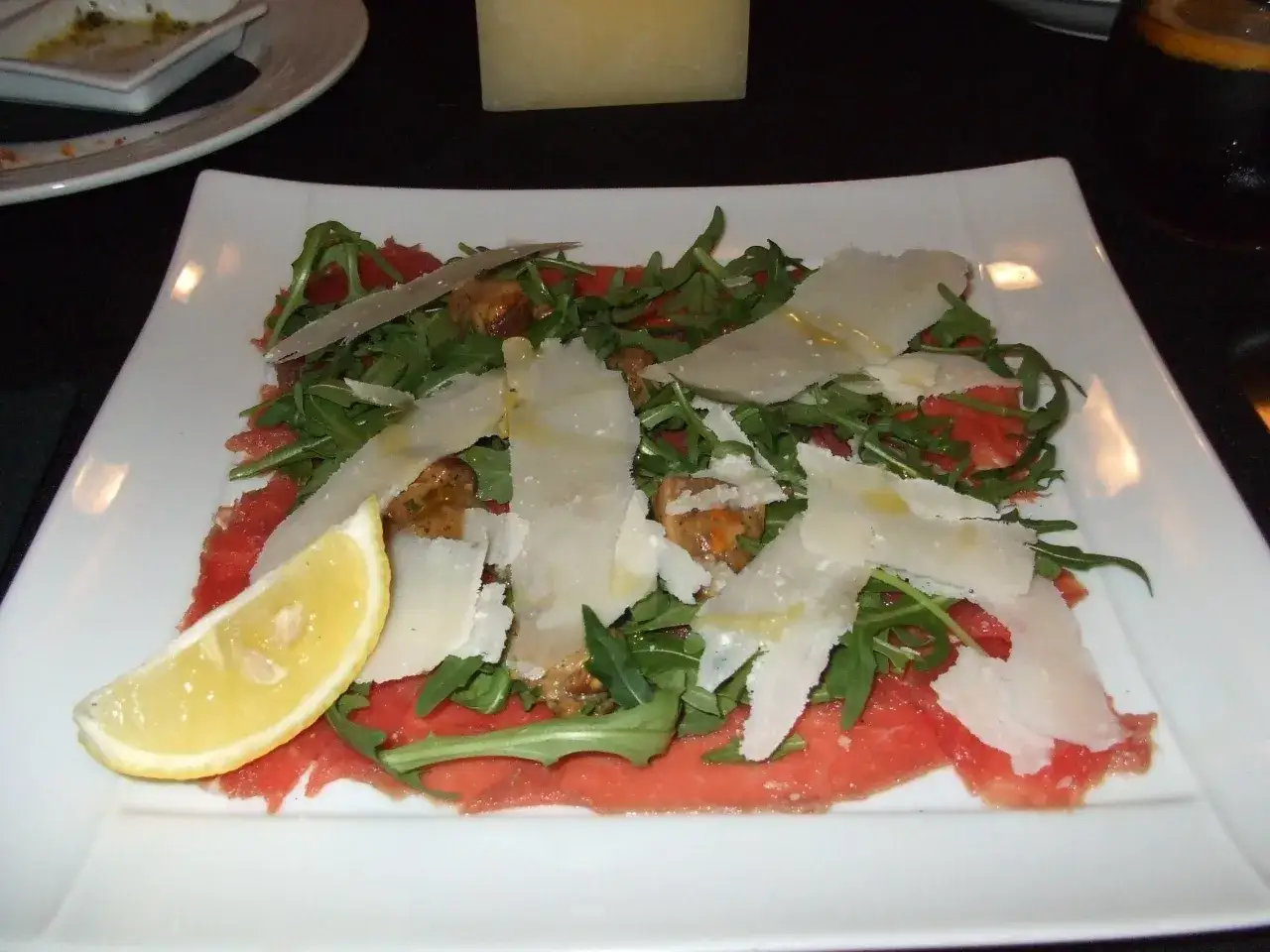 Delicato carpaccio di manzo con rucola, scaglie di parmigiano e una fetta di limone.