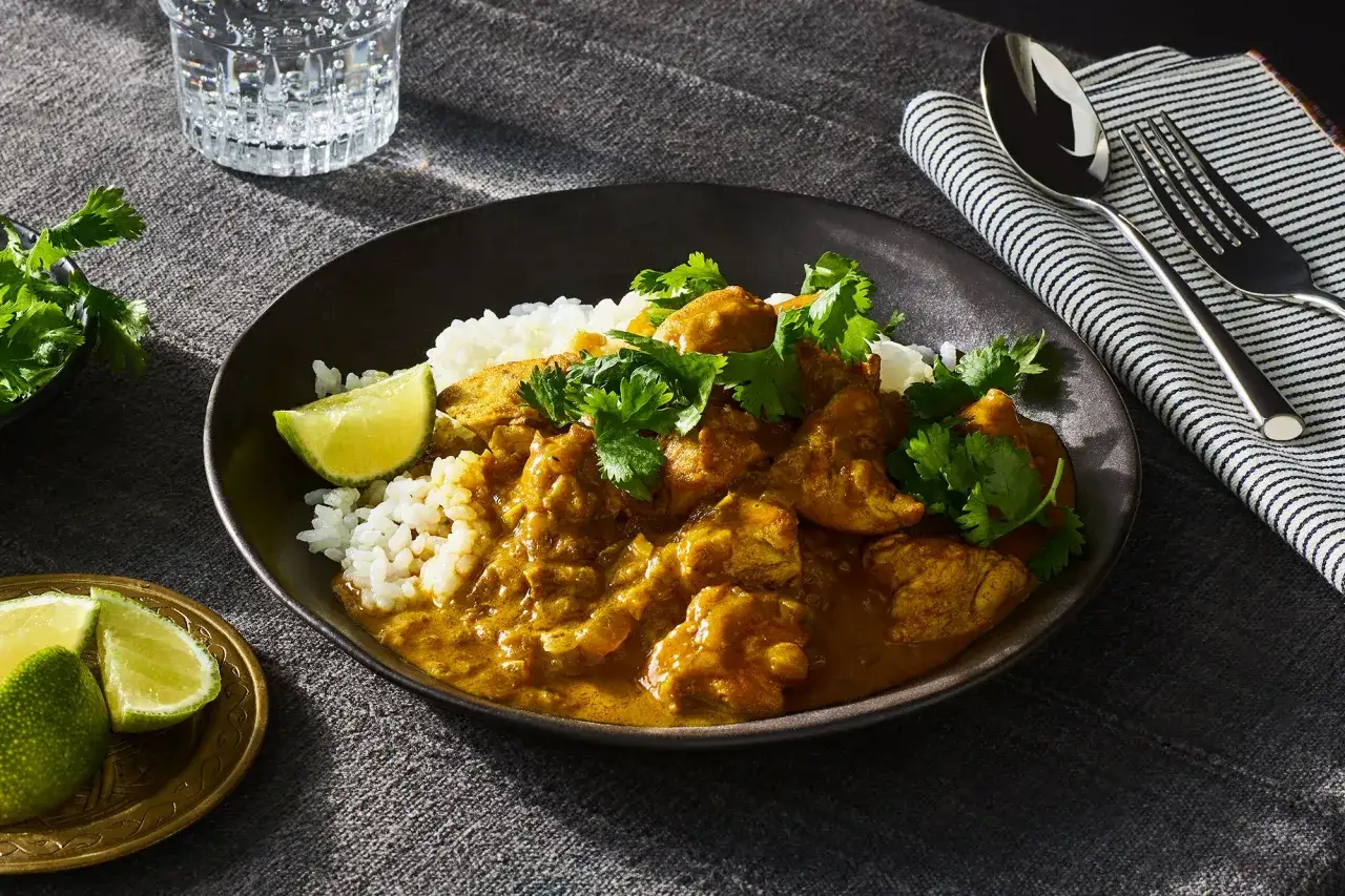 Un invitante pollo al curry servito su riso bianco, guarnito con coriandolo fresco e spicchi di lime.