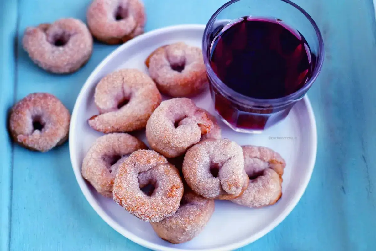 Ciambelline al vino, dolcetti friabili cosparsi di zucchero, accompagnati da un bicchiere di vino rosso.