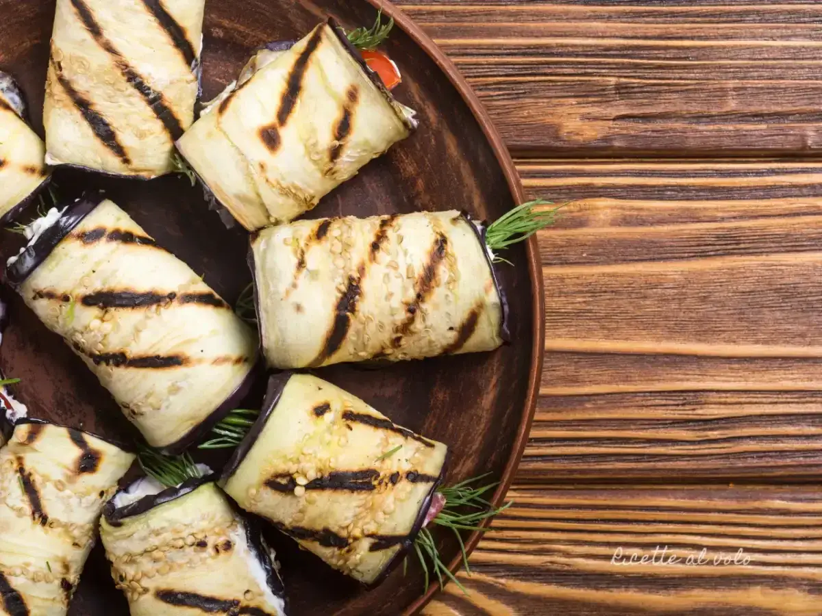 Involtini di melanzane grigliate ripieni di formaggio fresco e erbe aromatiche, serviti su un piatto di terracotta.