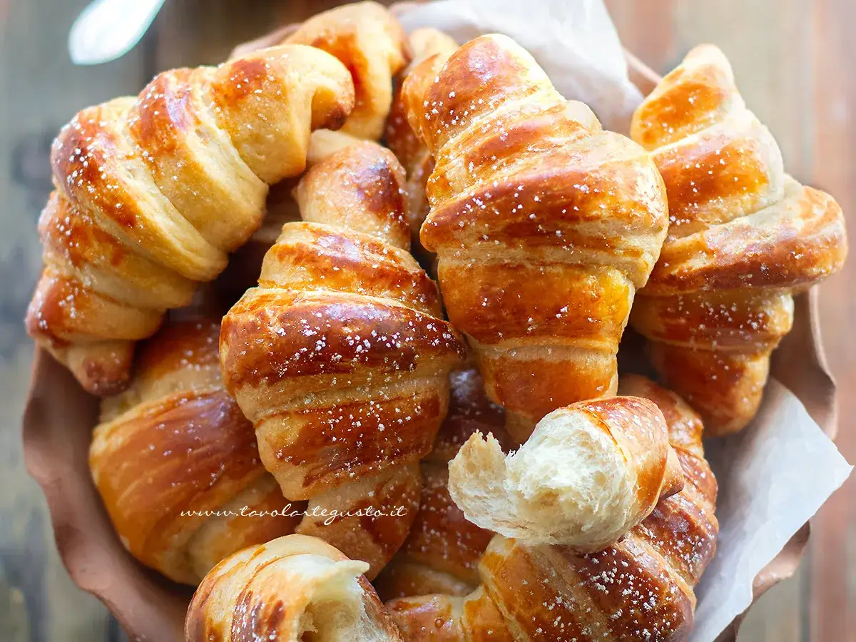 Cornetti fatti in casa dorati e soffici, spolverati di zucchero a velo, invitano a una colazione golosa.