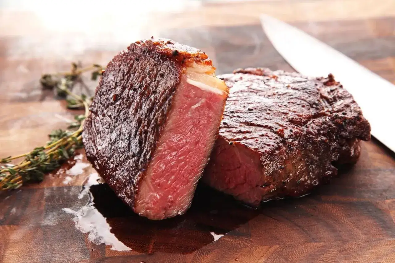 Costata di manzo succulenta, tagliata a met&agrave;, con un interno rosato e una crosta dorata. Accanto, un rametto di rosmarino e un coltello affilato.