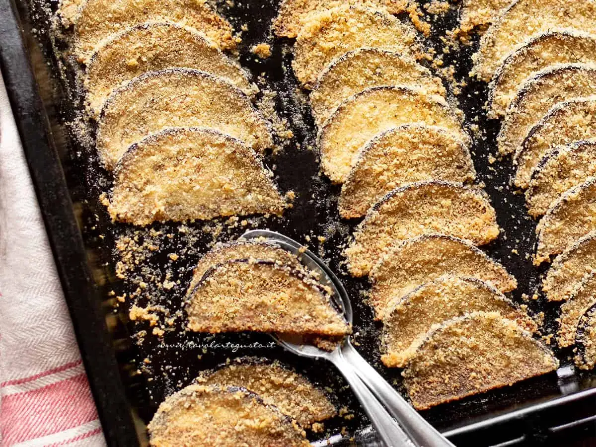 Fette di melanzane al forno, dorate e croccanti, disposte su una teglia.