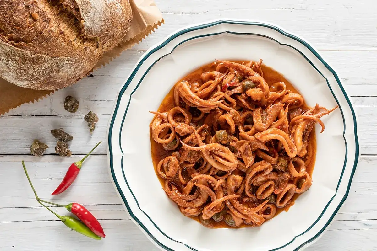 Piatto di totani in umido con capperi, peperoncino e pane rustico.