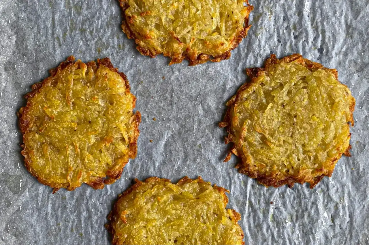 Quattro rosti di patate dorati e croccanti su carta forno.