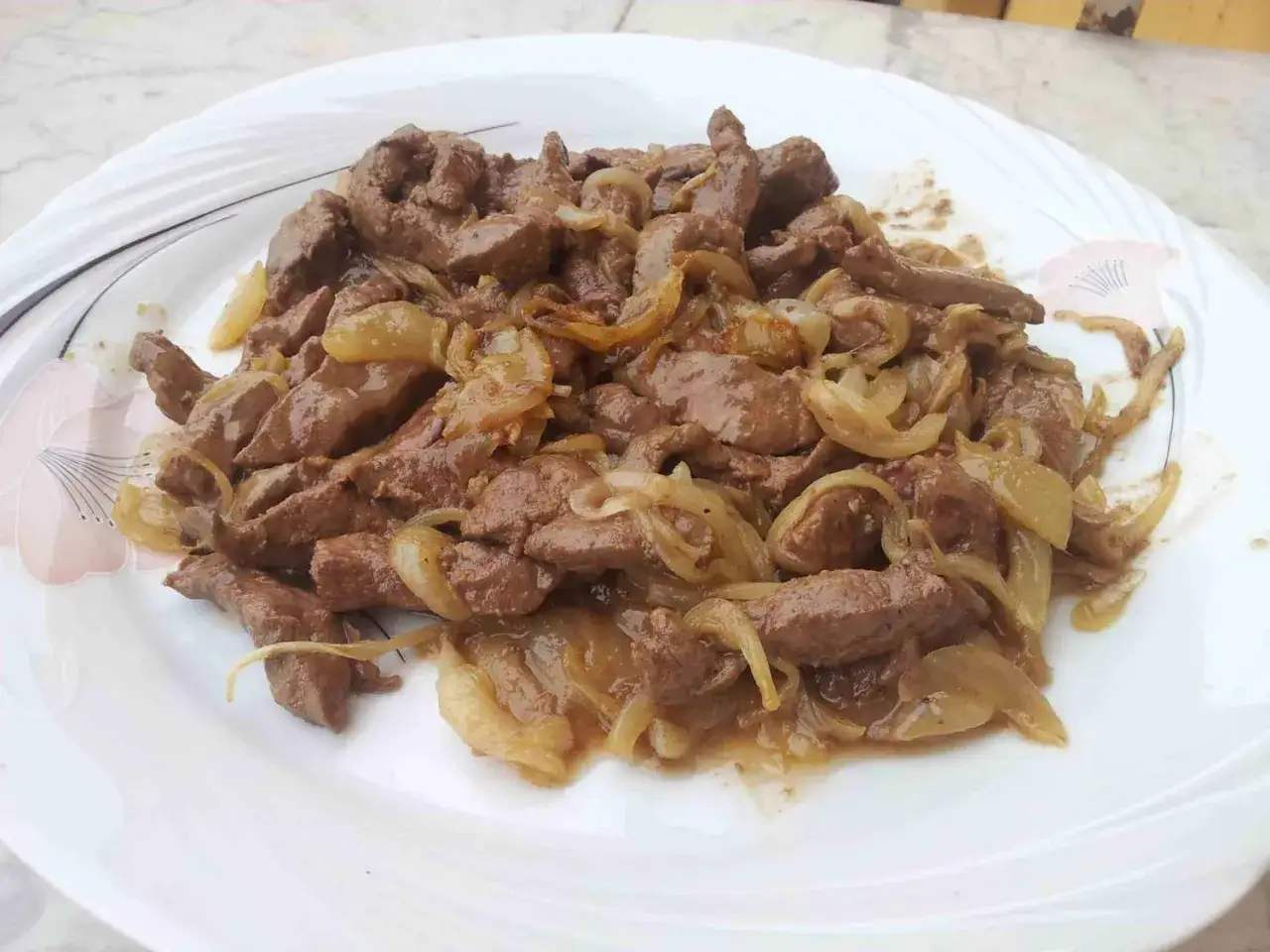 Piatto di fegato alla veneziana con cipolle caramellate, un classico della cucina veneta, servito su un piatto bianco decorato.