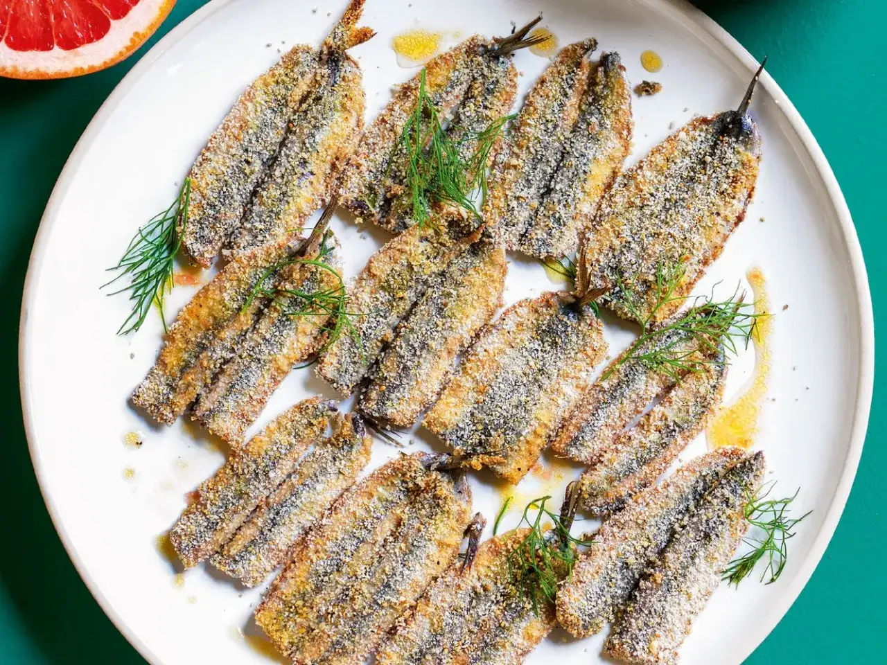 Piatto di alici al forno dorate e croccanti, guarnite con finocchietto fresco e un filo d'olio.