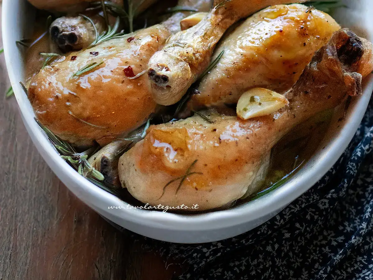 Succulente cosce di pollo al forno, dorate e profumate al rosmarino e aglio, servite in una ciotola bianca.