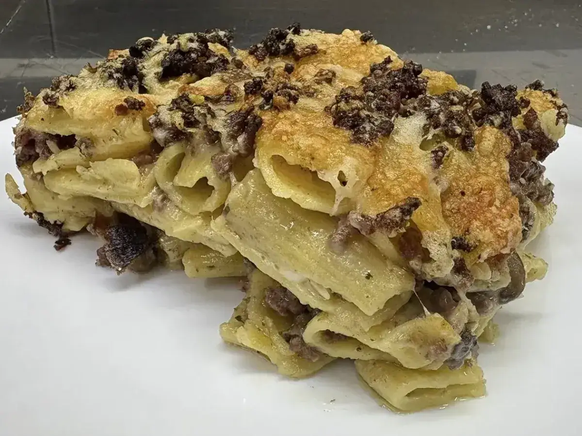 Porzione generosa di pasta al forno con ragù e formaggio fuso, dorata e invitante.