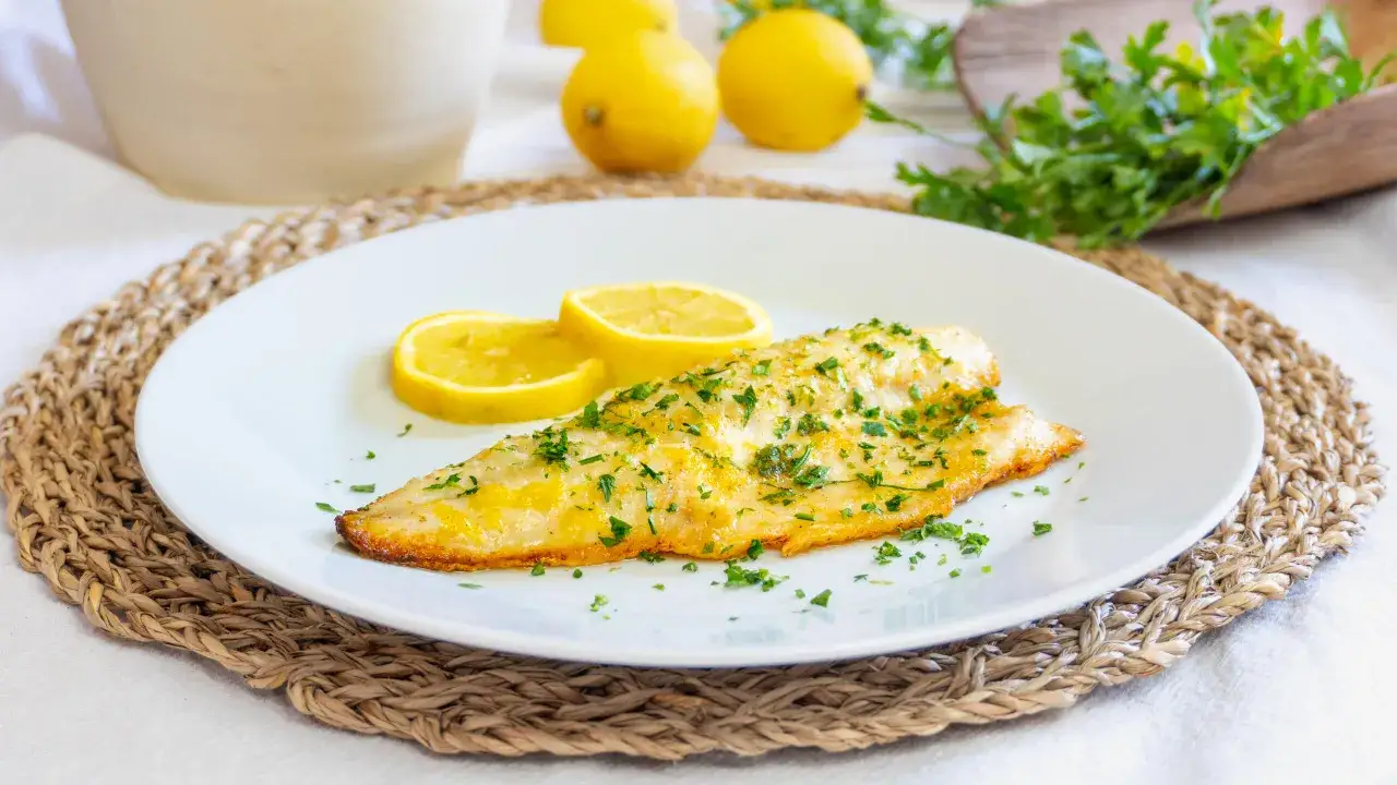 Delizioso branzino in padella, dorato e profumato, servito con spicchi di limone e prezzemolo fresco. Un piatto semplice e gustoso.