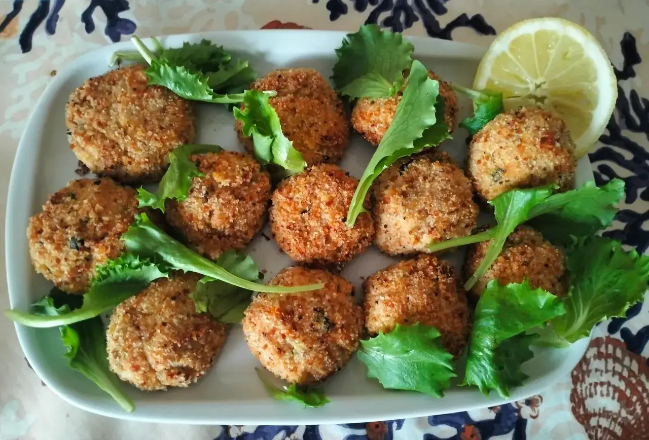 Deliziose polpette di tonno dorate e croccanti, guarnite con foglie di lattuga fresca e una fetta di limone.