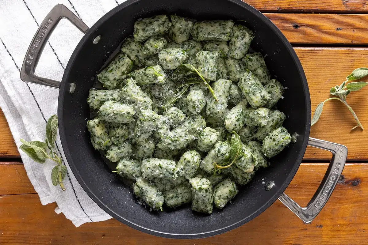 Strangolapreti alla trentina appena preparati, conditi con burro fuso, salvia e parmigiano, in una padella Le Creuset.