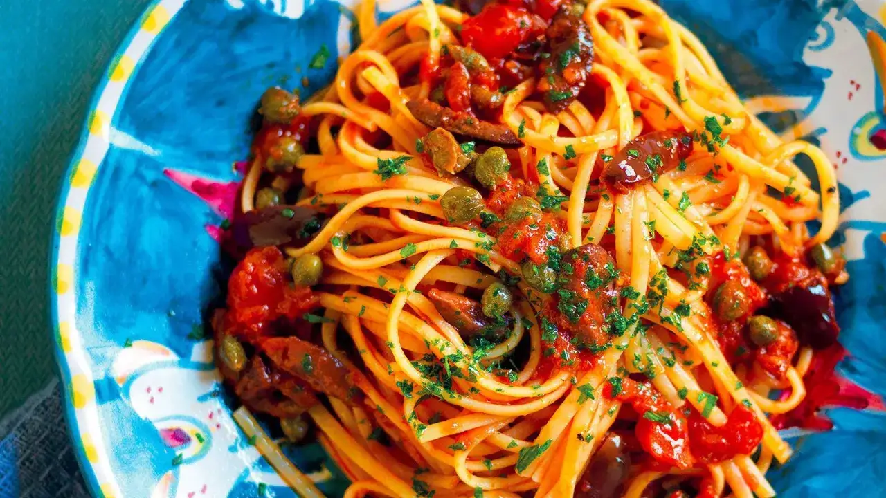Un piatto di linguine condite con un sugo rosso vivace, olive nere, capperi e prezzemolo tritato. Un'esplosione di sapori per la pasta alla puttanesca.