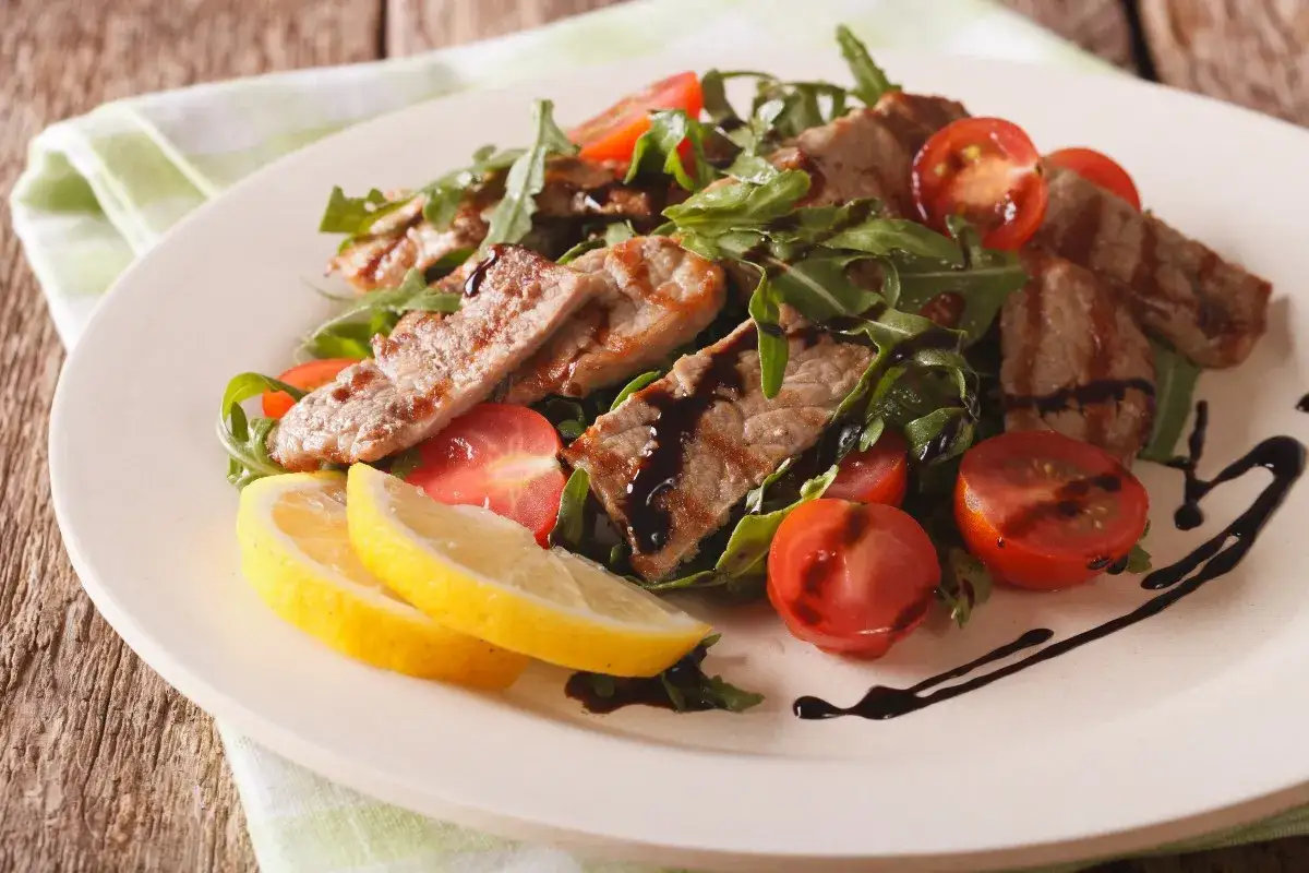 Deliziosi straccetti di vitello grigliati su un letto di rucola e pomodorini, guarniti con limone e glassa balsamica.
