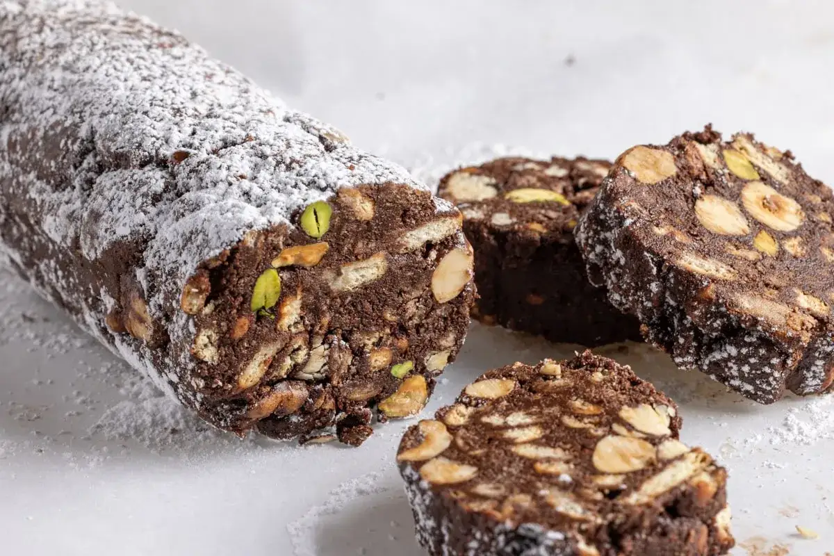 Salame di cioccolato senza uova, ricco di biscotti, nocciole e pistacchi, spolverato di zucchero a velo.