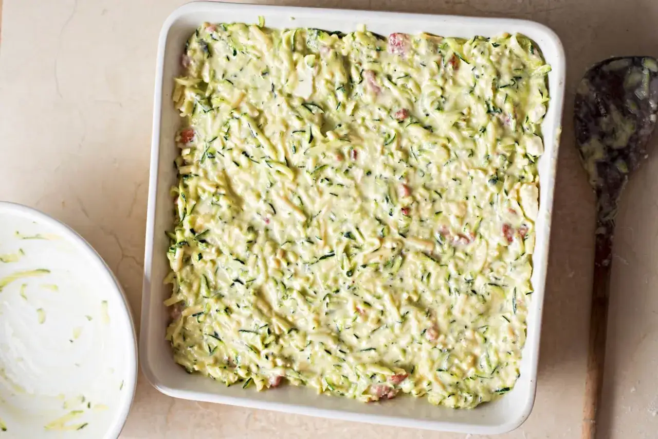 Sformato di zucchine pronto per essere infornato, con un mestolo sporco di impasto a lato.