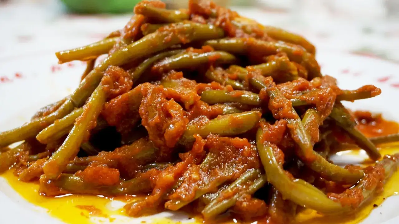 Un piatto invitante di fagiolini in umido, conditi con un sugo rosso saporito e un filo d'olio.