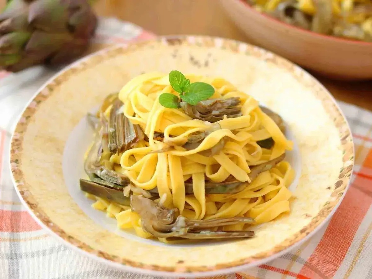 Un piatto di tagliatelle fresche con carciofi teneri, guarnito con una fogliolina di menta.