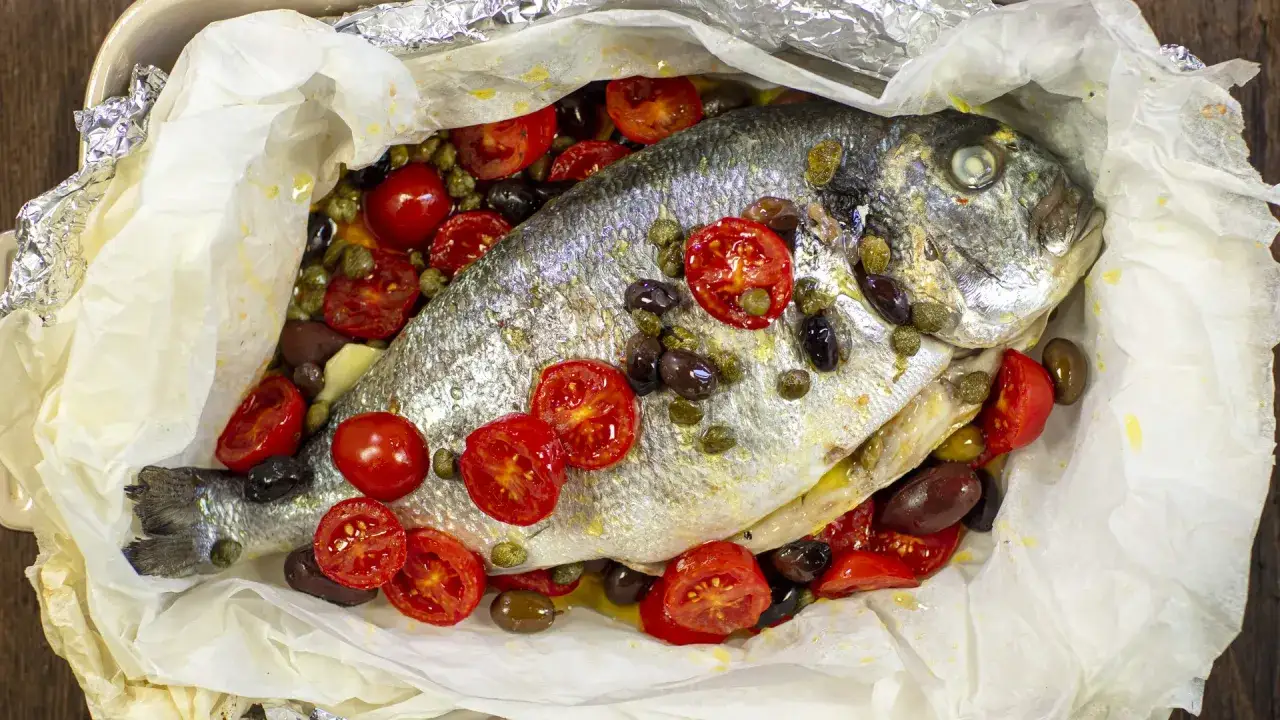 Orata al cartoccio con pomodorini, olive e capperi, un piatto saporito e profumato.