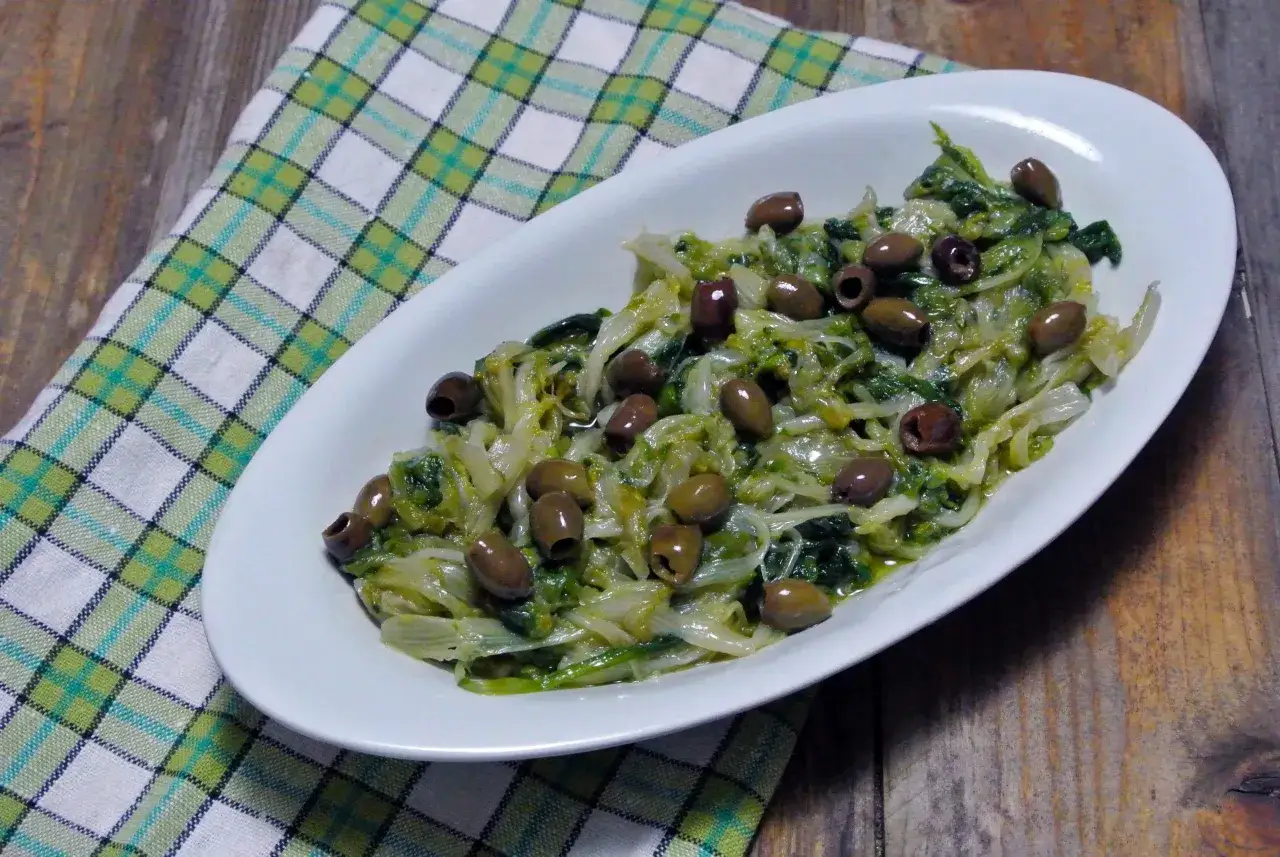 Scarola in padella con olive nere, un contorno saporito e salutare, servito su un piatto bianco con tovagliolo a quadri.