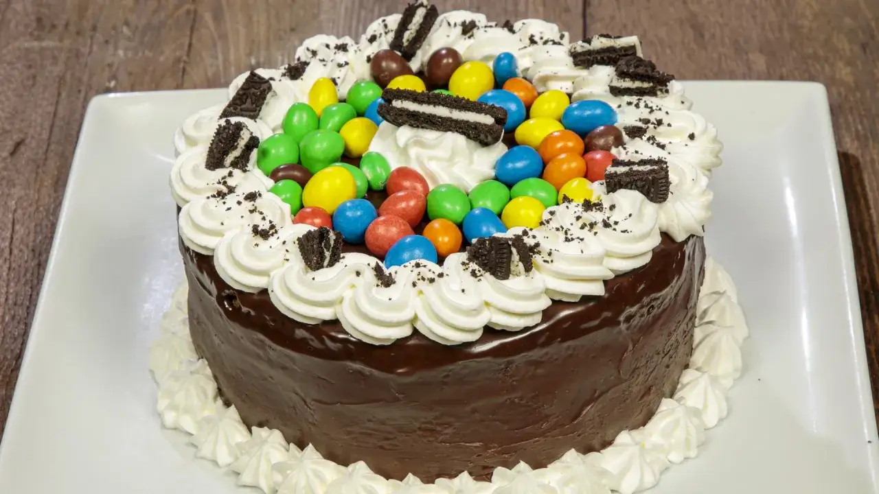 Torta al cioccolato con panna montata, caramelle colorate e biscotti Oreo, perfetta per i bambini.