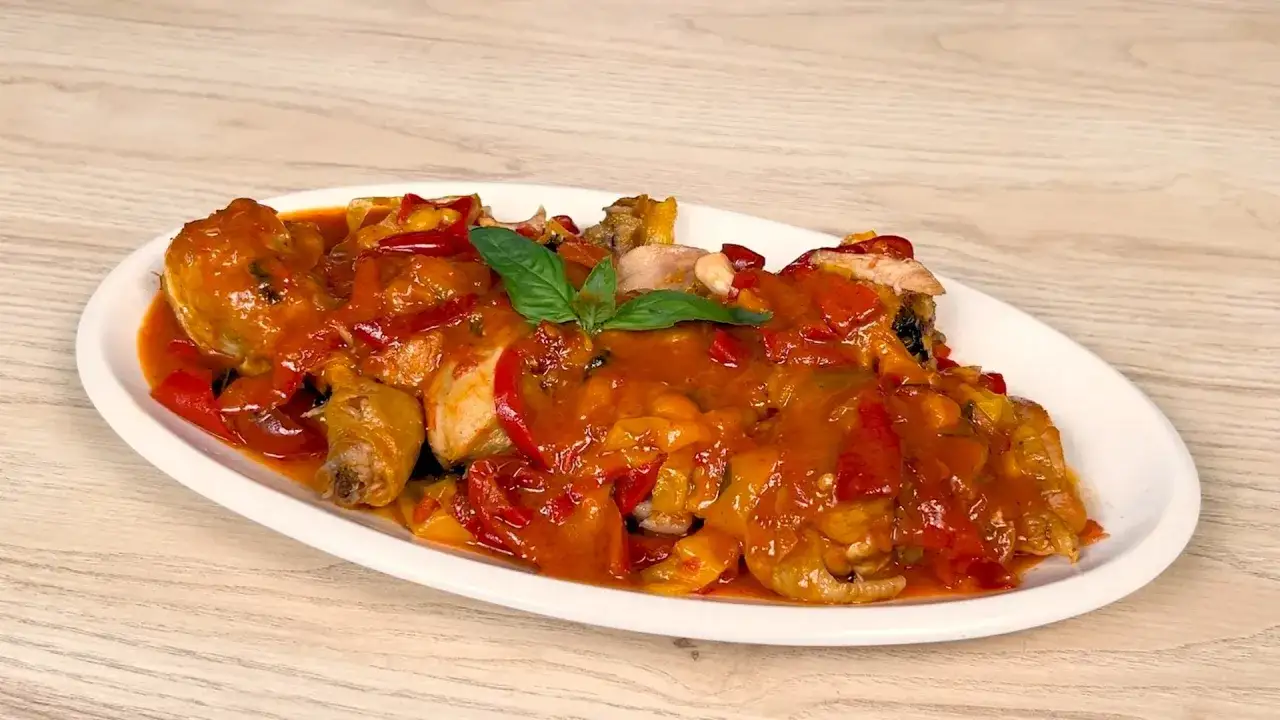 Pollo alla romana succulento con peperoni rossi e gialli, guarnito con basilico fresco su un piatto bianco.