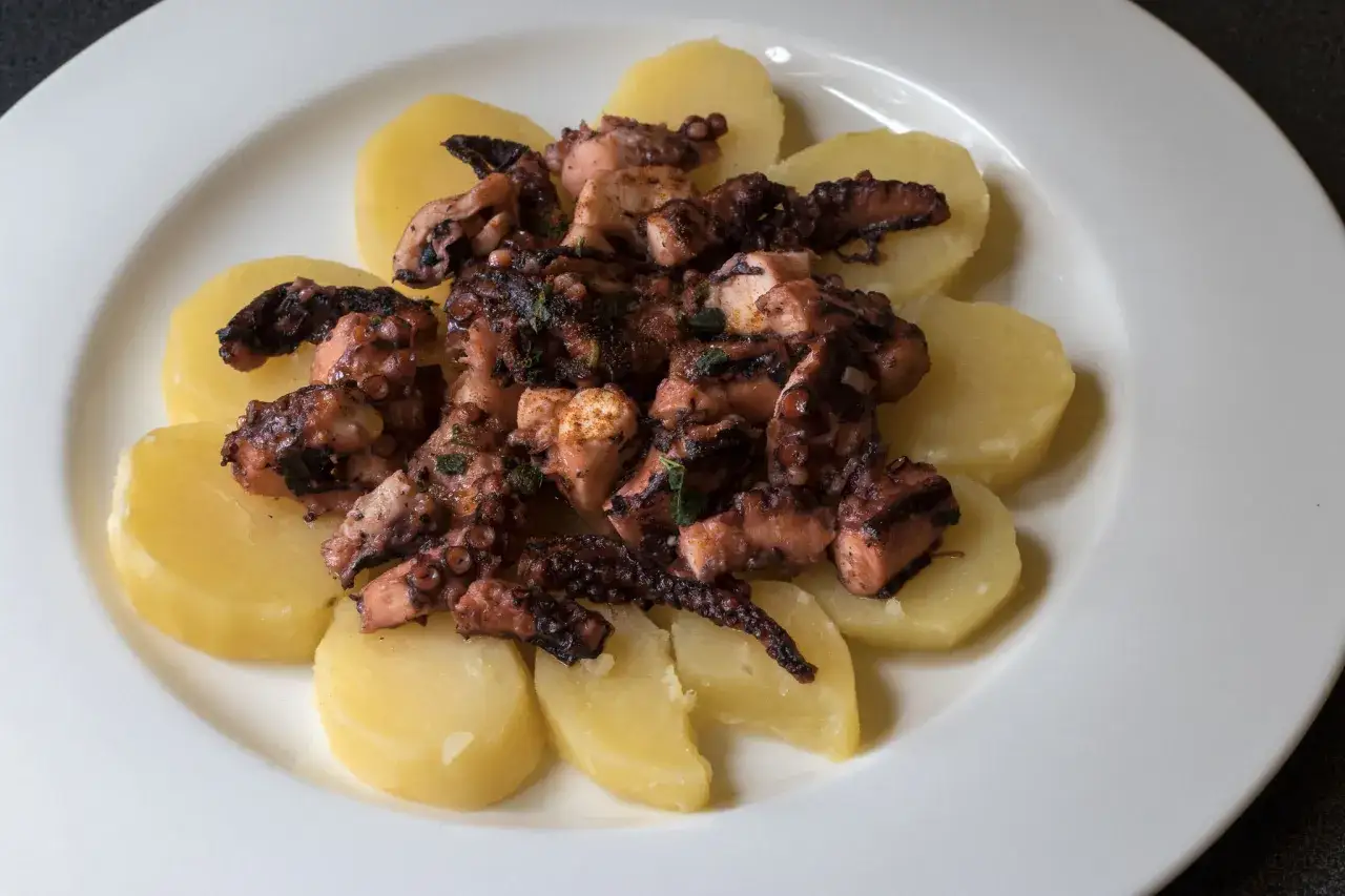 Piatto di polpo alla gallega su fette di patate bollite, condito con erbe aromatiche e spezie.