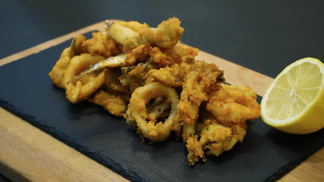Un invitante piatto di frittura di pesce, croccante e dorato, accompagnato da una fetta di limone fresco.