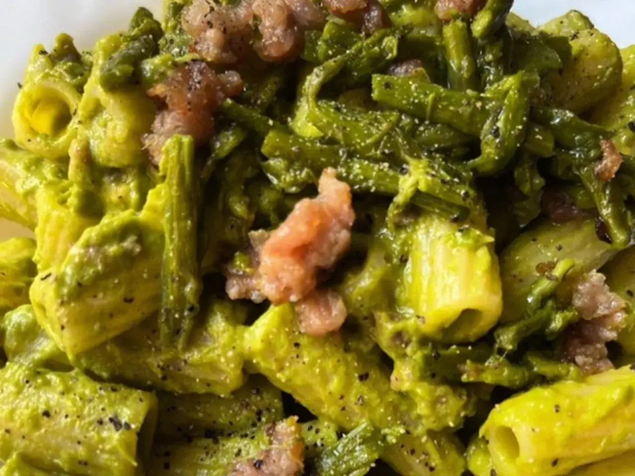 Primo piatto di pasta con asparagi e salsiccia, condito con una crema verde e pepe nero.