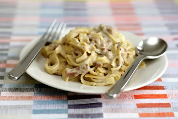 Un piatto di tagliatelle ai funghi cremose, con forchetta e cucchiaio pronti per gustare questo delizioso primo.