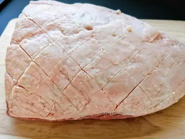 Un pezzo di picanha alla griglia, con la sua copertura di grasso incisa a rombi, pronto per essere cotto su un tagliere di legno.