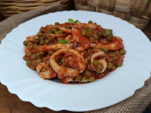 Un piatto invitante di seppie con piselli in umido, condito con una salsa rossa saporita e guarnito con basilico fresco.