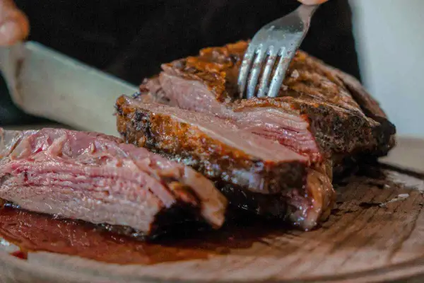Un succulento arrosto di maiale, tagliato a fette su un tagliere di legno, con una forchetta che affonda nella carne tenera.