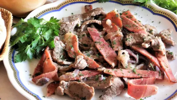 Straccetti di manzo con pancetta e cipolla, guarniti con prezzemolo fresco. Un piatto saporito e invitante.