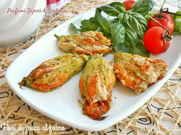 Deliziosi fiori di zucca al forno ripieni, serviti su un piatto bianco con pomodorini e basilico fresco.
