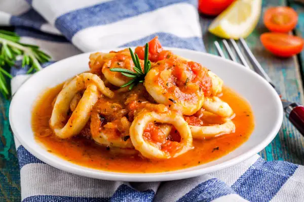Calamari in umido succulenti, cotti in una salsa rossa saporita, guarniti con rosmarino fresco.