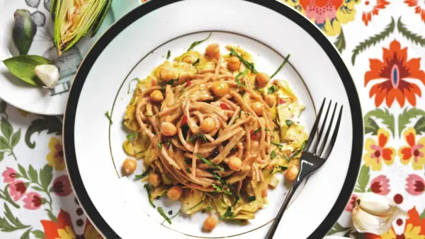 Un piatto invitante di pasta con carciofi alla siciliana, arricchito da ceci e erbe fresche, su un tovagliolo colorato.