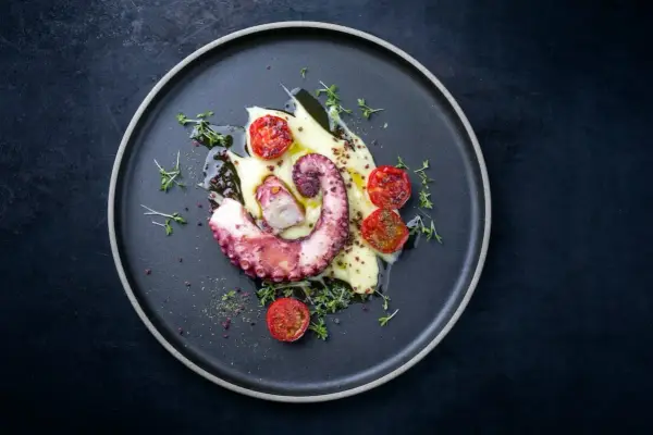 Un tentacolo di polpo alla griglia, servito su purè di patate con pomodorini confit e timo fresco.
