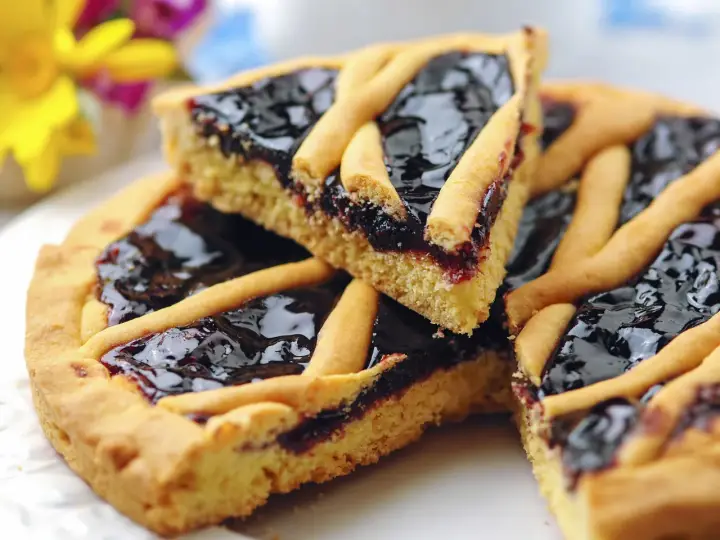 Una fetta di crostata di marmellata, con la sua base dorata e il ripieno scuro e lucido, pronta per essere gustata.