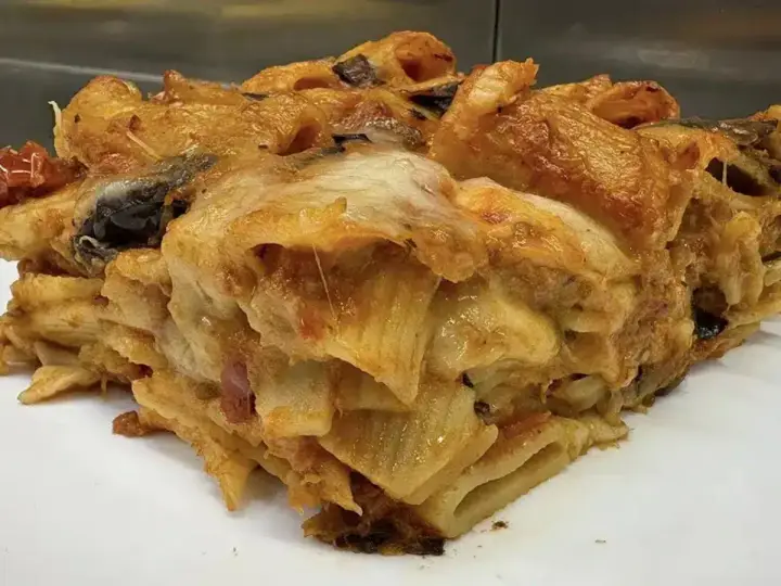 Una fetta di pasta al forno ricca e dorata, con strati di pasta, melanzane e formaggio filante.