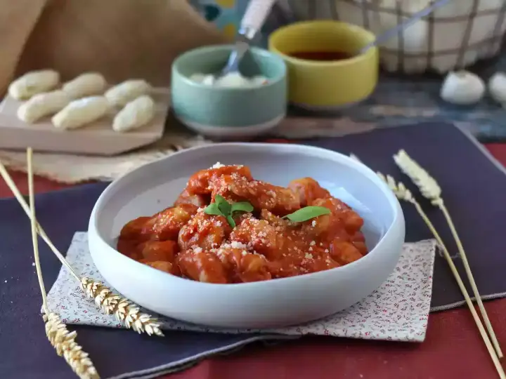 Un invitante piatto di gnocchi alla sorrentina, conditi con sugo rosso e parmigiano, guarniti con basilico fresco.
