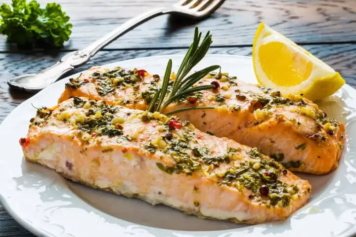 Delizioso salmone al forno con erbe aromatiche, aglio e peperoncino, guarnito con rosmarino e una fetta di limone.